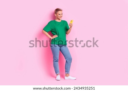 Full size photo of pleasant adorable girl dressed green t-shirt jeans look at smartphone read email isolated on pink color background