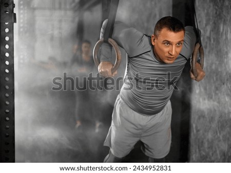 Adult athletic man in sportswear training with gymnastic rings in gym