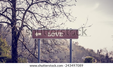 Signpost with pointing arrow towards Love in front of a bare branched tree with mountain backdrop.