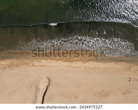 Overhead drone view of the serene interaction between gentle waves and the soft sandy beach, creating a peaceful coastal rhythm