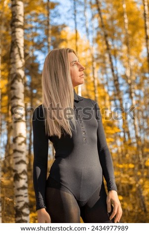 A beautiful girl in a black outfit stands in the autumn forest against a background of trees. The scene is serene and peaceful, the girl is enjoying nature.