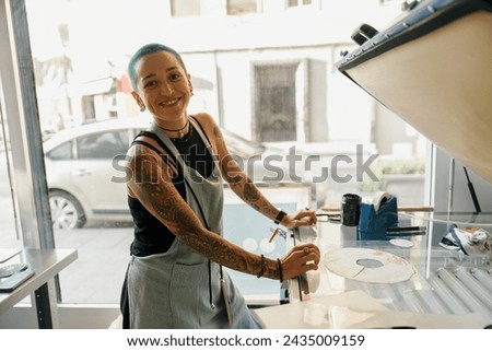 Smiling female worker preparing screen printing film while using printing machine in a workshop