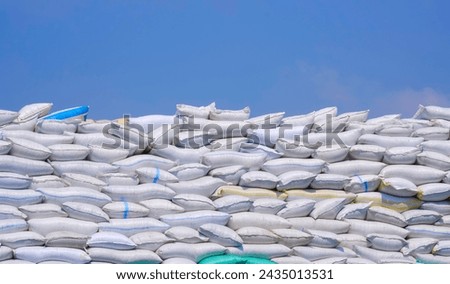 Many sacks of crushed plastic bottles or bottle flakes stacked on industrial yard area against blue sky background, recycling used plastic material to new synthetic fiber concept Royalty-Free Stock Photo #2435013531