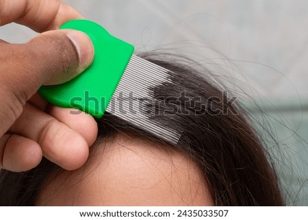 a close-up of hand meticulously combing through hair with a green fine-toothed comb, targeting the removal of lice nits. the process exemplifies a common method in personal hygiene and lice treatment