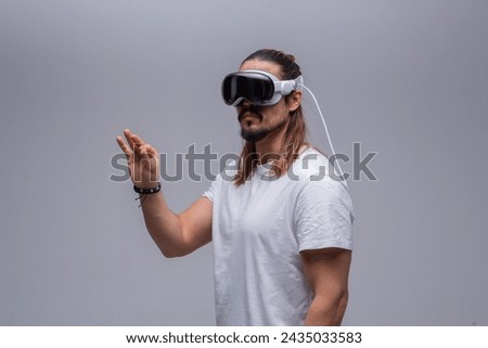 A young man engages with a virtual world using a mixed reality spacial computer headset, symbolizing cutting-edge technology in gaming and immersive digital experiences.  Royalty-Free Stock Photo #2435033583
