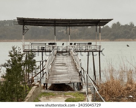 A small lake resembling the letter "T", with a picturesque pier surrounded by lush greenery. This tranquil scene invites relaxation and contemplation, offering a serene getaway amidst nature's beauty.