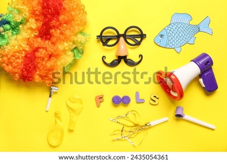 Word FOOLS with funny glasses, party decor and megaphone on yellow background