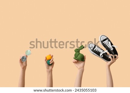 Female hands holding shoes with toy bunny, sunglasses and Easter eggs on beige background. Holiday travel concept