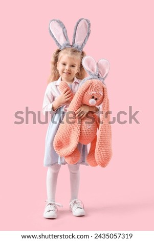 Cute little girl with bunny ears and plush toy on pink background. Easter celebration