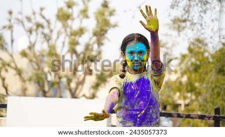 Young cute cheerful little girl kid with applied holi colors powder showing colorful hands to camera during holi festival celebration