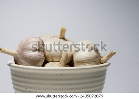 A bundle of fresh garlic bulbs sits in a white ceramic bowl, their papery skins ready for peeling