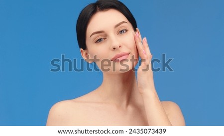 Face of a woman with blue eyes applying cream to her face and looking at the camera. Beautiful female model with perfectly clean fresh skin. Skin care or cosmetic advertising concept Royalty-Free Stock Photo #2435073439