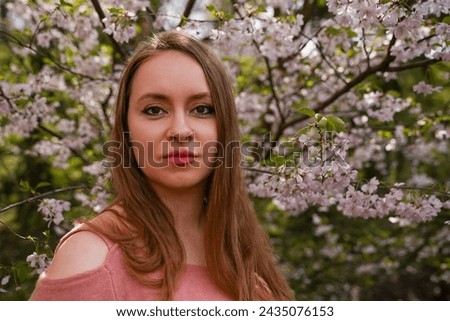 beautiful blond natural hair woman in pink outfit, posing in botanical garden park near blooming sakura tree with flowers. Spring and purity, natural beauty. International women's day