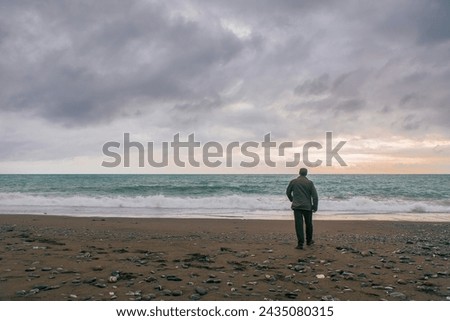 Solitary man standing by the seaside and staring in the distance. He's wearing a military outfit and is not recognizable.