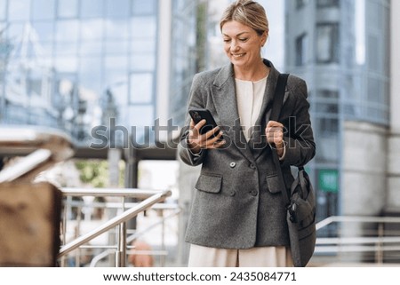 Portrait of a beautiful mature business woman in suit and gray jacket smiling and talking on the phone on the modern urban background