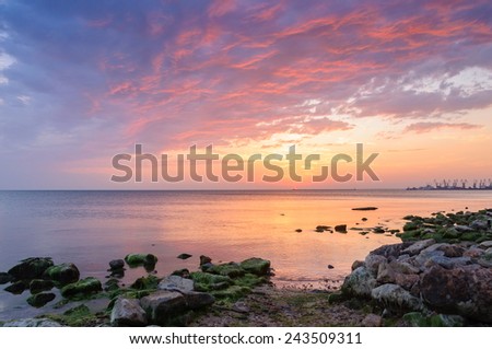 The picture was taken on a city beach during sunset near a sea port.