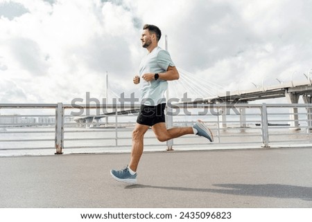 Man jogging on a sunny day with a bridge in the background, focused on his fitness goals.

