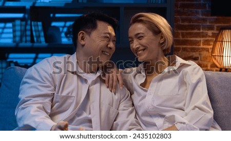 Multiracial couple Asian man and Caucasian woman family diverse girlfriend and boyfriend adult wife and husband watching TV enjoy funny television program laugh movie laughing at home at late night Royalty-Free Stock Photo #2435102803