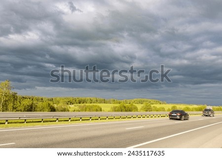paved road surrounded by fields, against a dramatic sky background.
