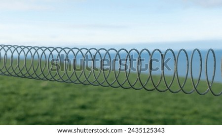 Springy fence in green field by blue sea horizon