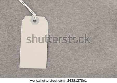 Cardboard tag on brown garment, top view. Space for text