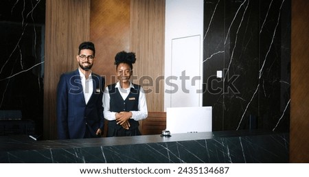 Portrait of polite, professional male and female workers of fancy hotel in uniform. Indian and African-American hotel managers smiling and looking into the camera. Customer care concept. Royalty-Free Stock Photo #2435134687