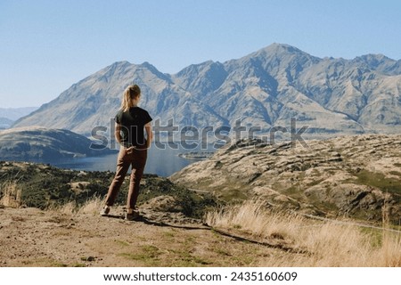 Woman looking out at tall layered NZ mountains and calm water