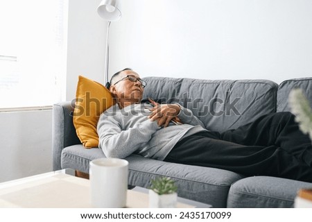 Elderly Asian man wear glasses, sleeping on couch at home after tired reading a book Royalty-Free Stock Photo #2435170099