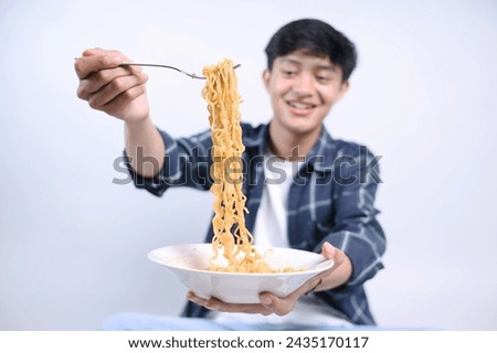 Young Asian man showing noodles to camera with happy expression, selective focus