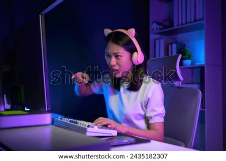 Excited and smiling Asian gamer girl in cute headset playing an online video game in her bedroom.