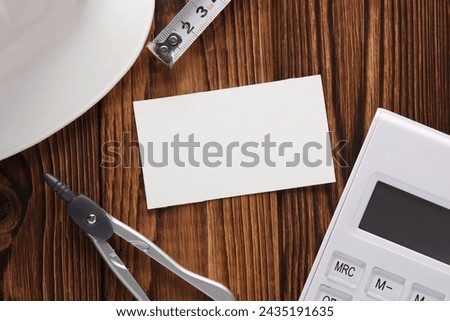 Engineer's tools and white blank business card on wooden boards. Top view