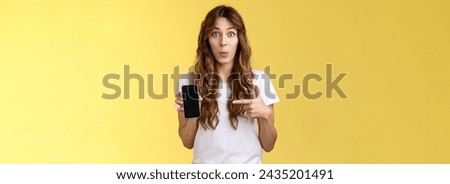 Intriguing app check out. Enthusiastic surprised attractive girlfriend gossiping friend new boyfriend showing curious photo smartphone hold mobile phone pointing telephone screen yellow background.