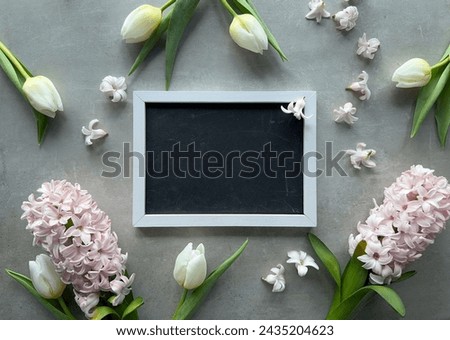 A wooden picture frame placed on a table, encircled by fragrant spring flowers, white tulips and pink hyacinth.