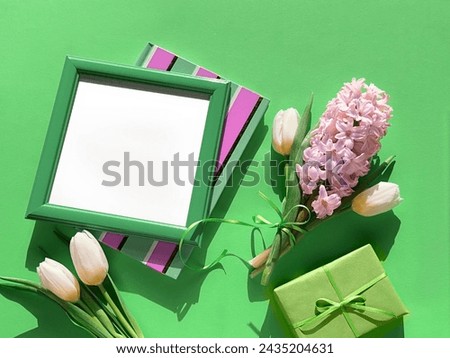A picture frame and gift box are next to a fragrant bouquet of spring flowers, featuring white tulips and pink hyacinth in full bloom.