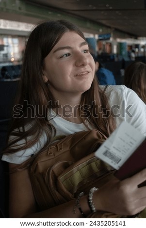 A teenager smailing, looking through airport window with her travel documents and backpack