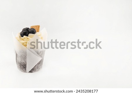 On a white background with space for writing text, the cupcake is decorated with cream, cookies and blueberries.