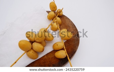 Date palm fruits and white cheesecloth are placed on a wooden cutting board. Tropical fruit with a rustic-style image on a white background. Date palm or palm fruit texture. Top view food image. Royalty-Free Stock Photo #2435220759