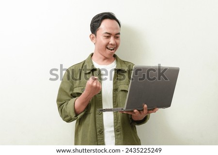 portrait of asian man holding and looking at laptop screen with smile face. Indonesian man in green shirt on isolated background. illustration of a businessman, entrepreneur, freelancer or student