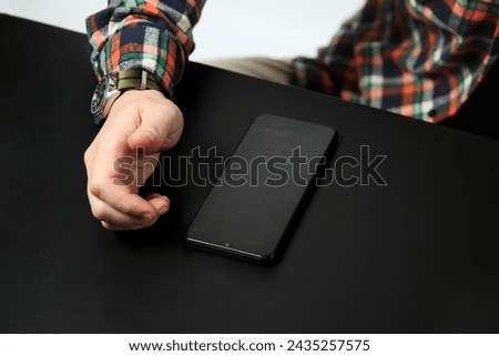 Black phone and male hand on the black table. Business concept. Top view. Close up. Royalty-Free Stock Photo #2435257575