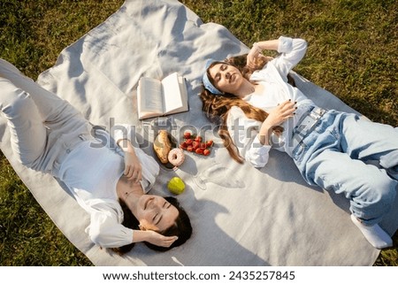 Young women spend time on picnic. Best friends relax and enjoy sunny summer lying on blanket with different sweets and talking Royalty-Free Stock Photo #2435257845