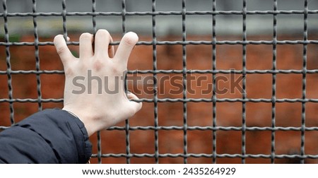 Iron bars of a reformatory and the hand of a young man clinging to the fence Royalty-Free Stock Photo #2435264929