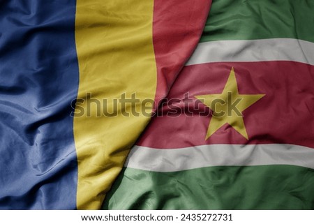 big waving national colorful flag of suriname and national flag of romania . macro
