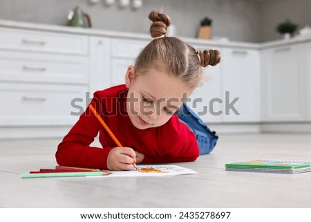 Cute little girl coloring on warm floor in kitchen. Heating system