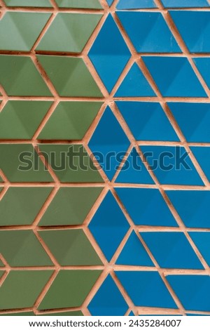 Striking pattern creating by meticulously arranged blue and green triangular tiles on concrete light wall. Optical illusion of depth and movement on texture