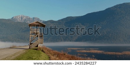  Morning at mountain lake with birdwatching tower                               Royalty-Free Stock Photo #2435284227