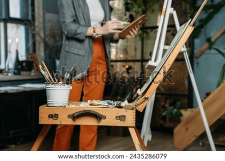 Painter working in real studio with oil paints and brushes, creating canvas, modern art. Young woman over window, closeup
