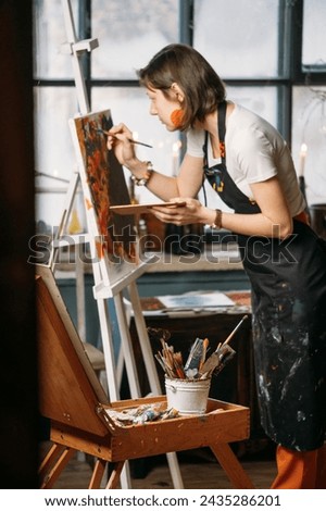 Painter working in real studio with oil paints and brushes, creating canvas, modern art. Young woman over window, closeup