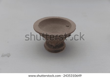 This image features an ancient terracotta oil lamp, a significant artifact from the Mohenjo-Daro archaeological site, set against a neutral background, highlighting its historical value