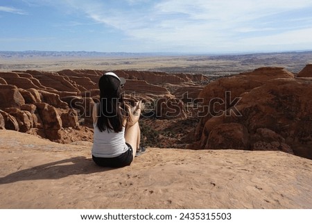 Woman in a cap captures the grandeur of a vast red rock canyon under the expansive blue sky, an iconic desert landscape.
