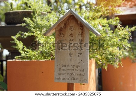 Japanese style wooden sign with messages written in Japanese. English and Thai, which is translated as written: let things go if you want to find peace in your mind, to give ideas to readers. Royalty-Free Stock Photo #2435325075